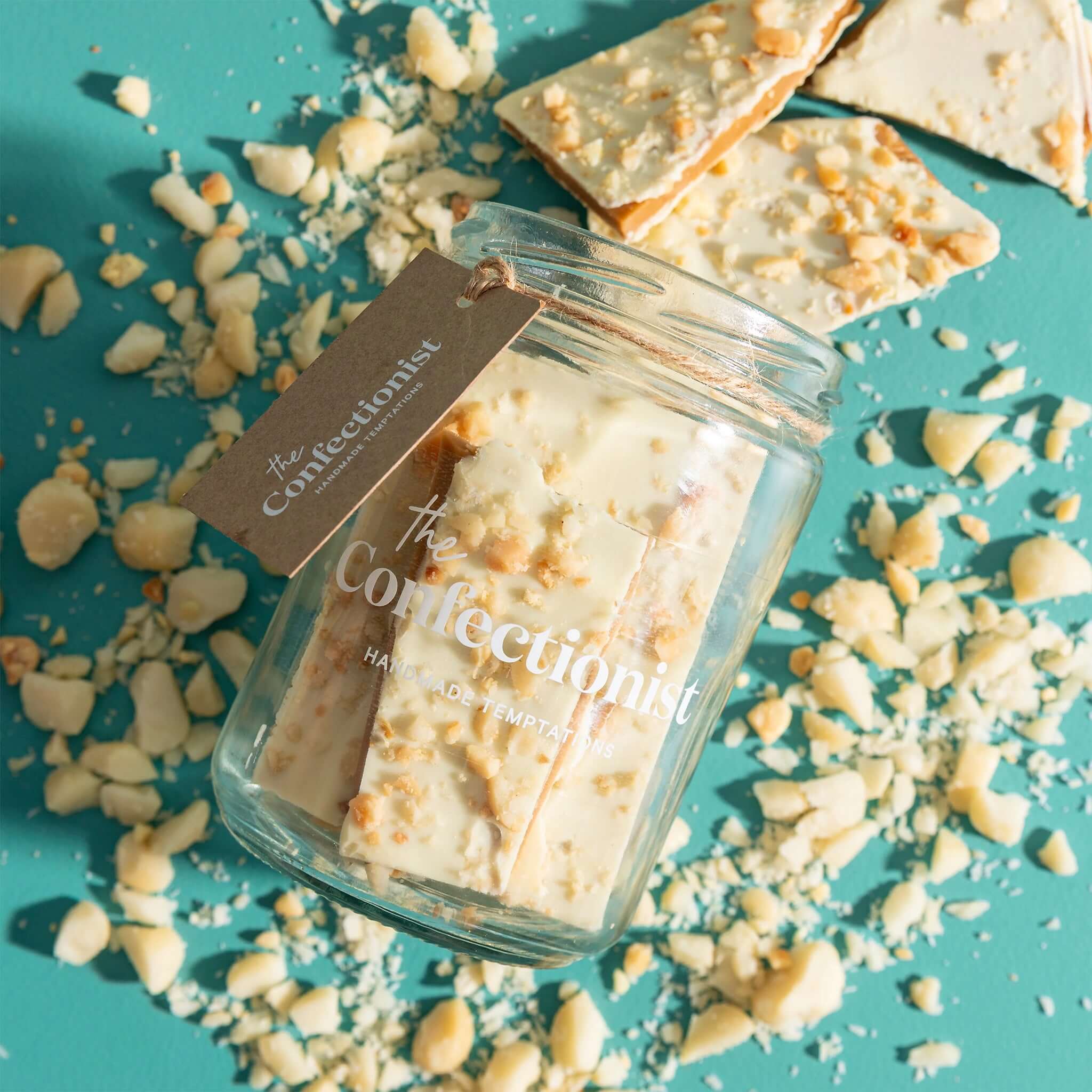 The Confectionist Limited Edition White Chocolate, Macadamia & Lemon Toffee - Large in a glass jar with broken pieces.
