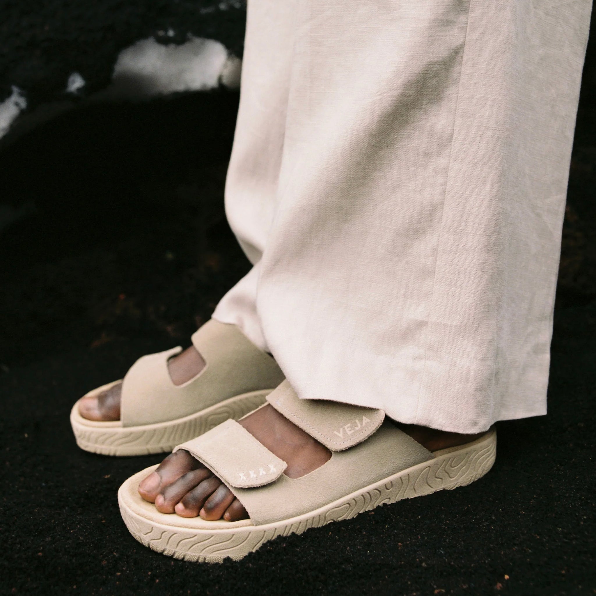 Beige sandals worn with light-colored pants on a dark background
