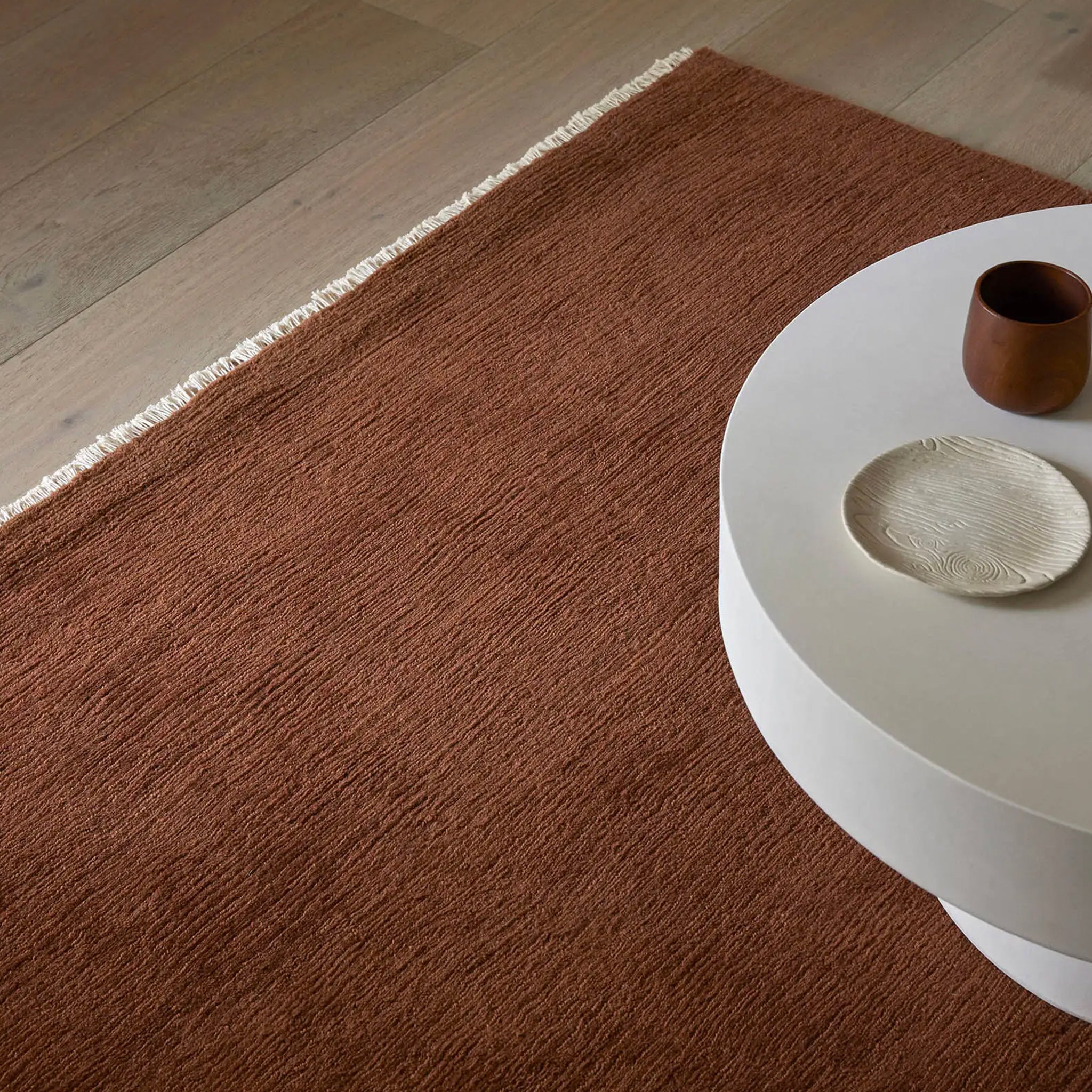 Brown rug on a wooden floor with a white round table and decorative items.