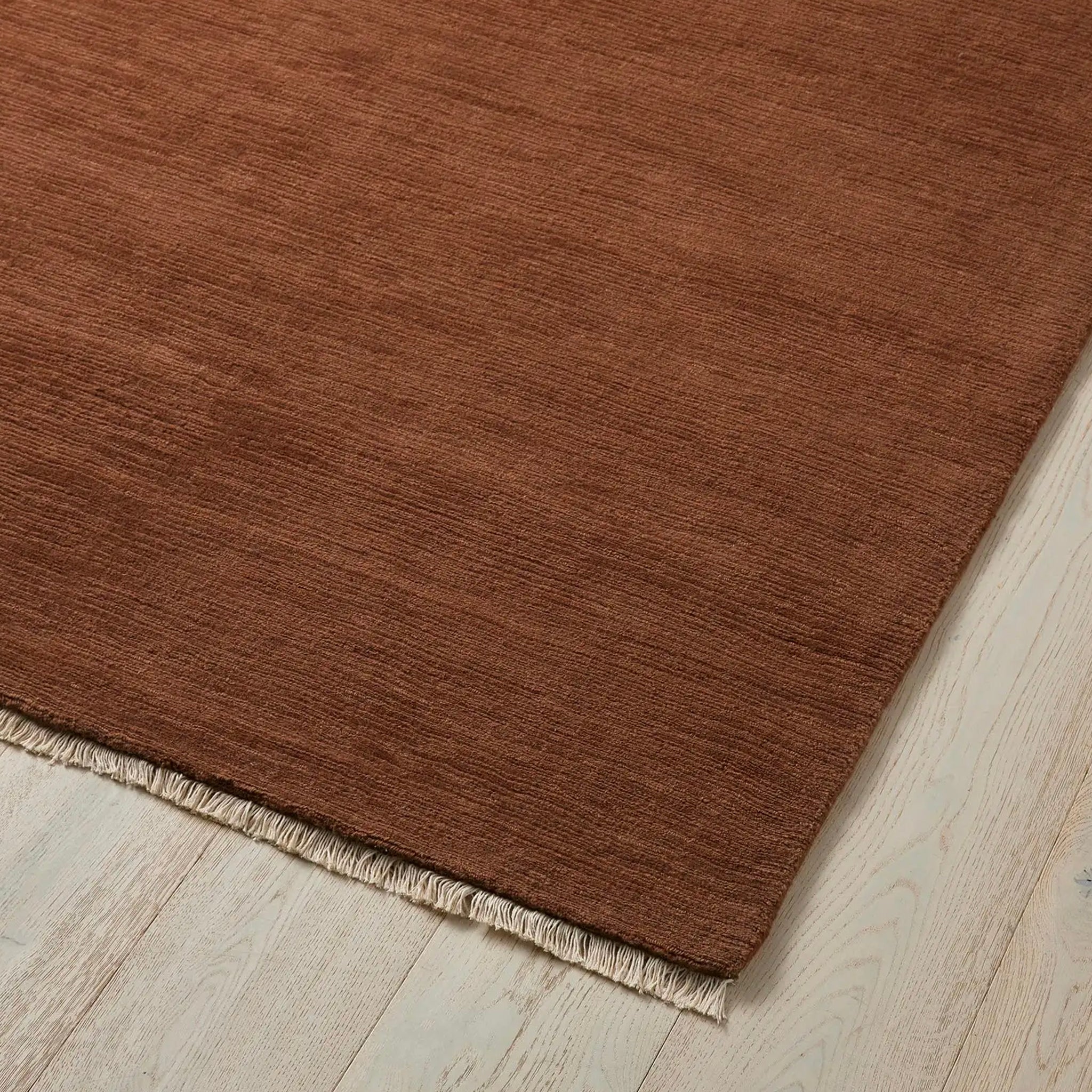 Brown rug with frayed edge on a light wood floor