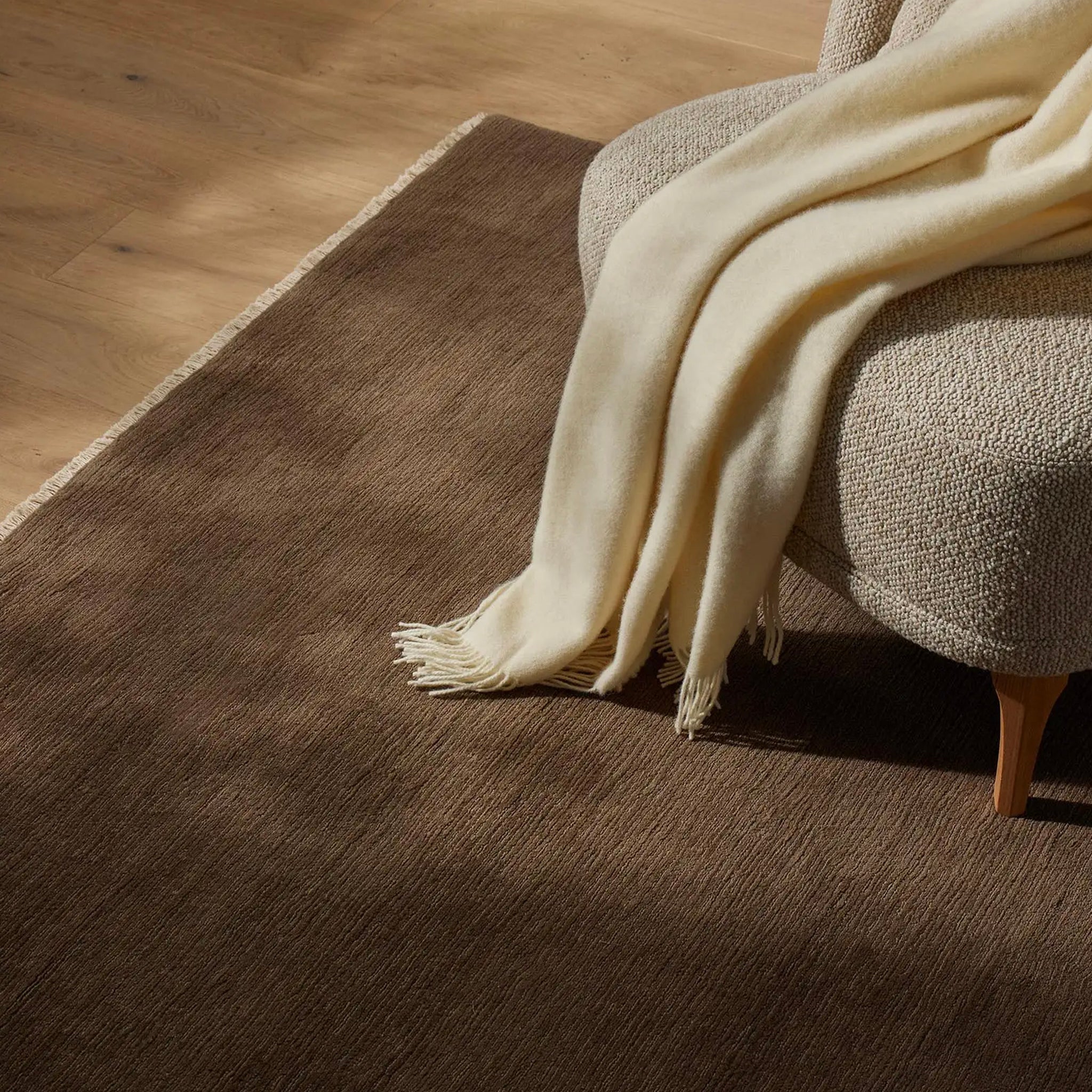 Beige blanket draped over a textured chair on a wooden floor