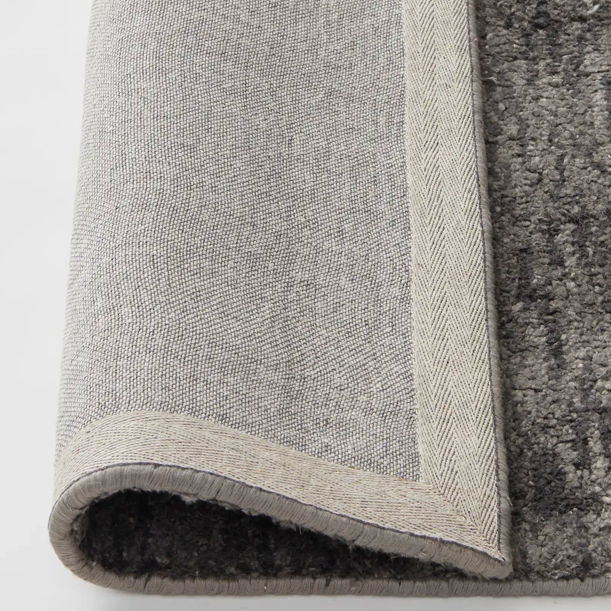 Close-up of a textured gray rug corner on a white background