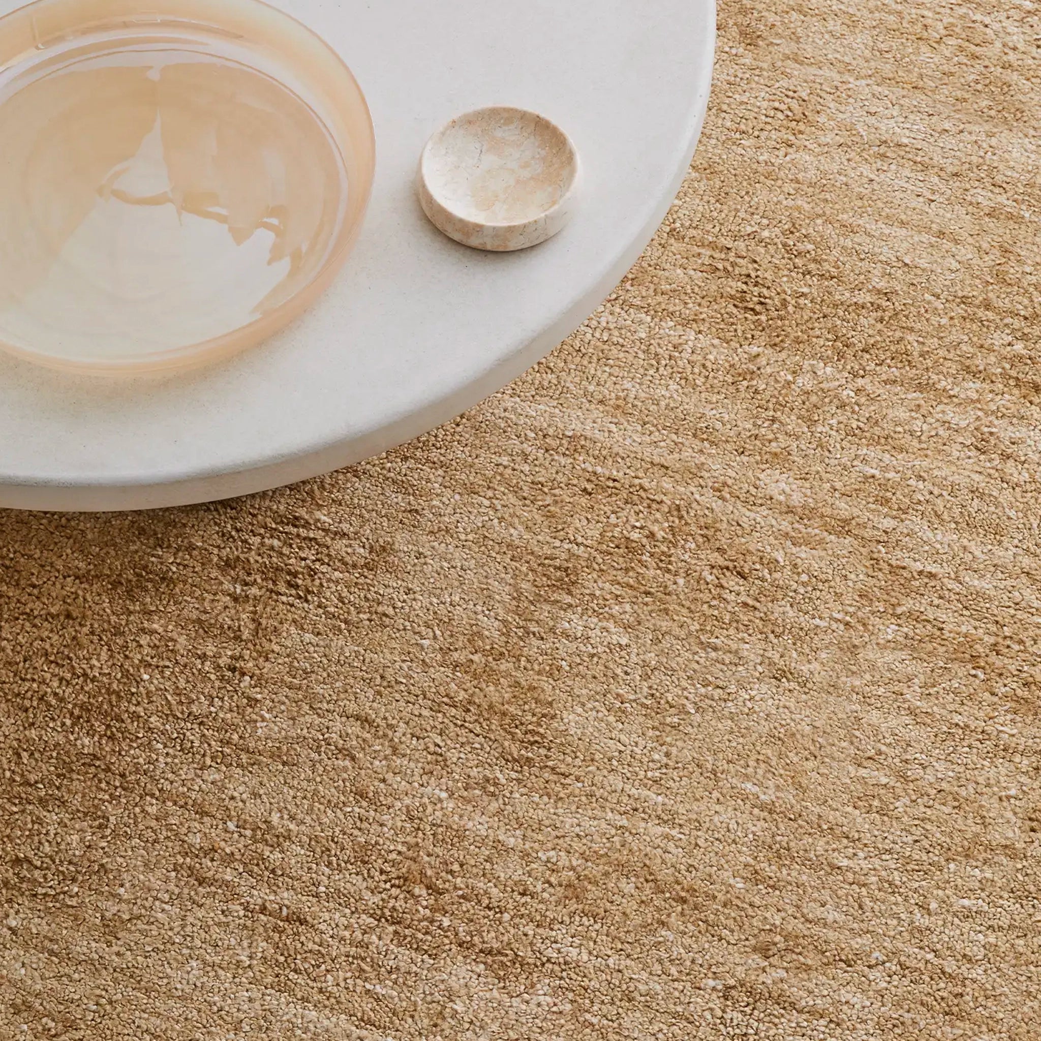 Close-up of a beige carpet with a white table and small bowl on a light background