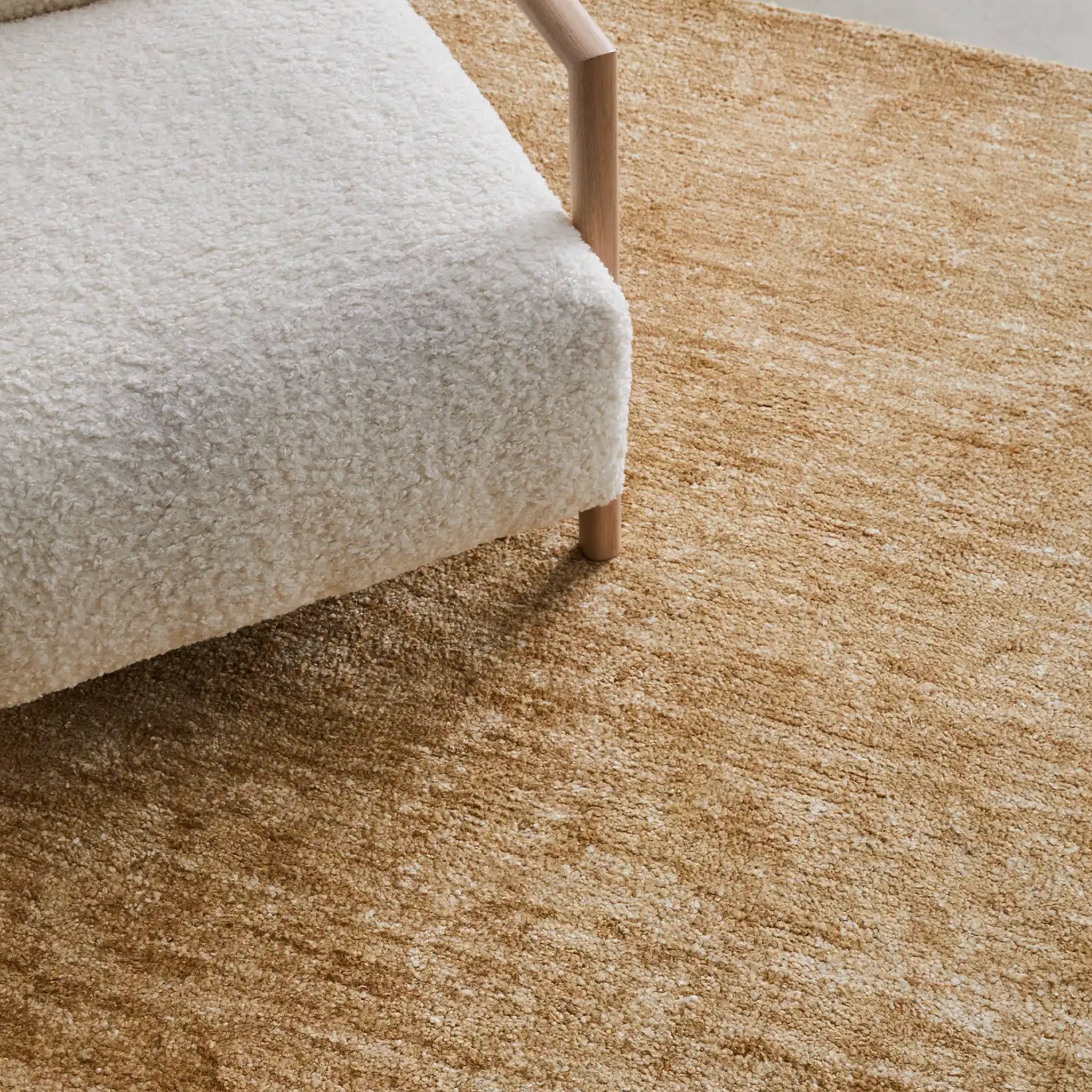 Beige carpet with a corner of a light gray upholstered chair.