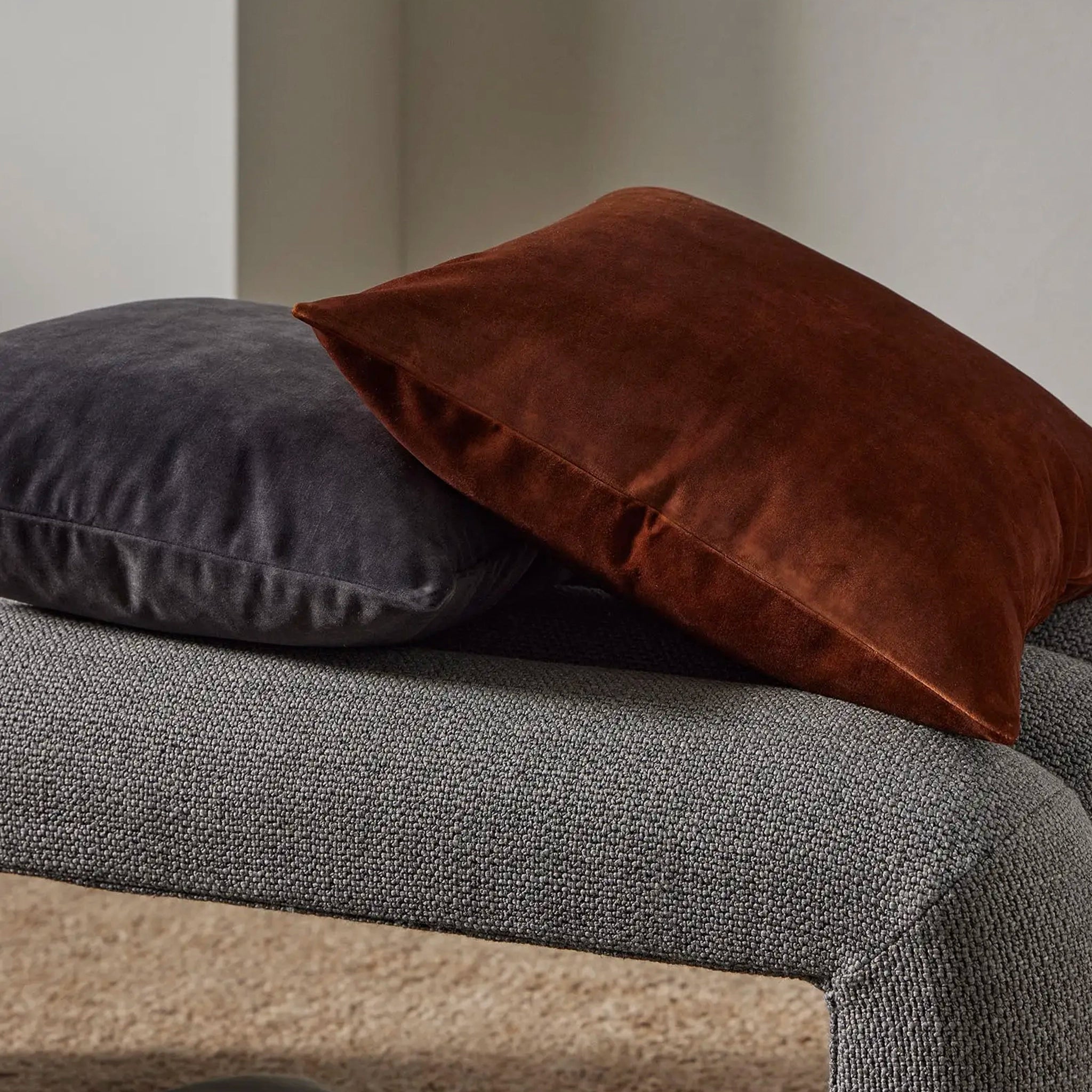 A grey and a brown velvet cushion on a white background.