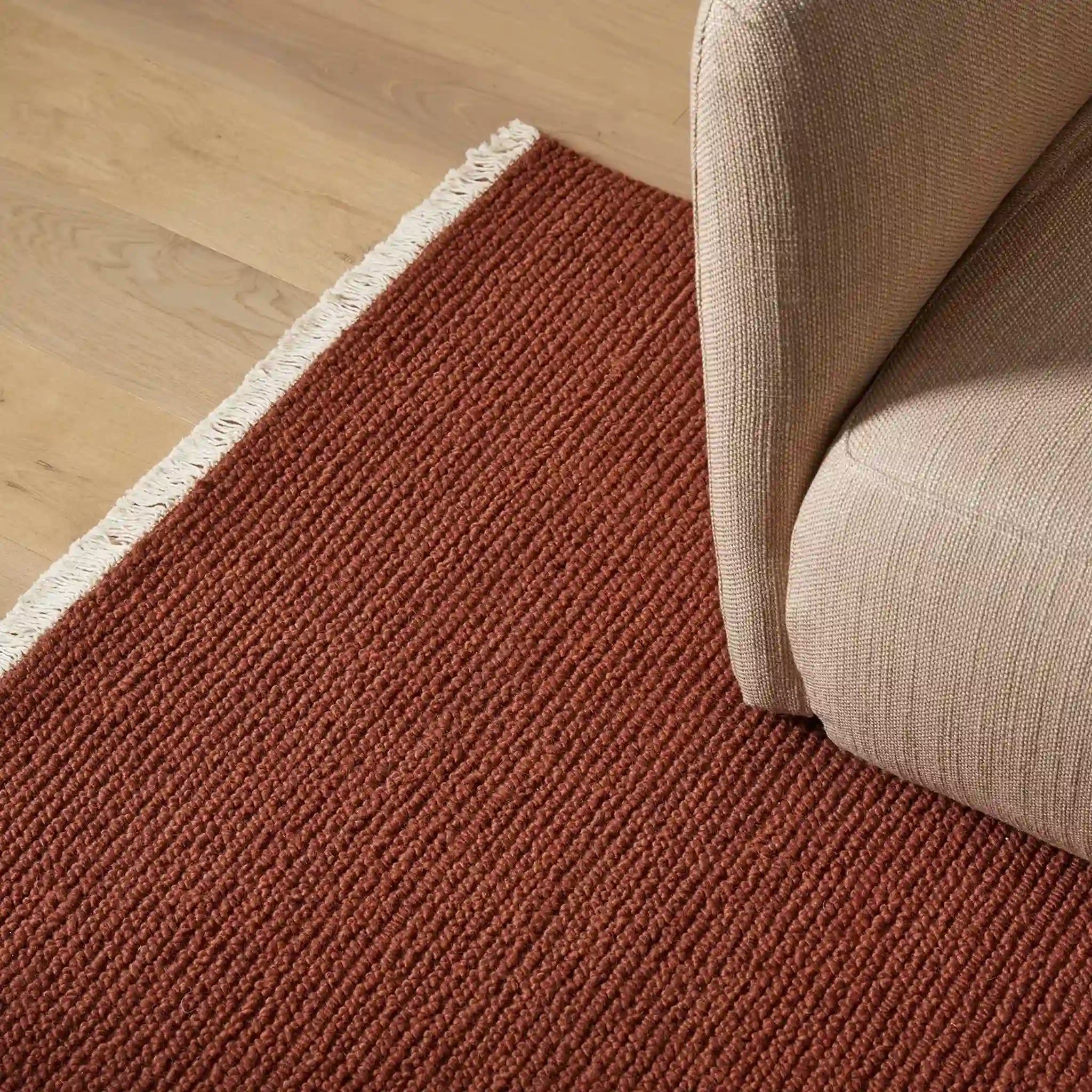 Brown textured rug on a wooden floor with a beige sofa corner.