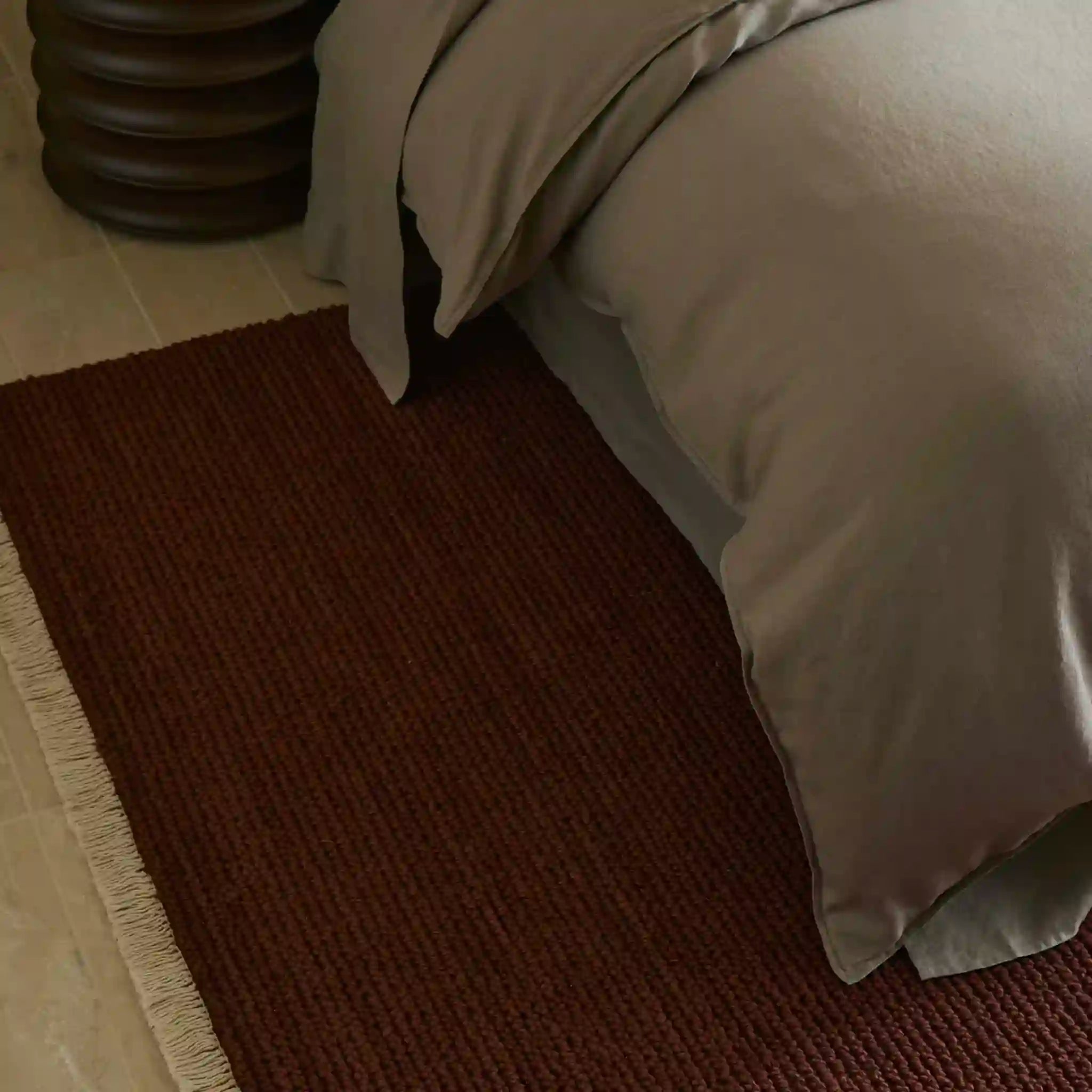 Brown rug in front of a bed with beige bedding