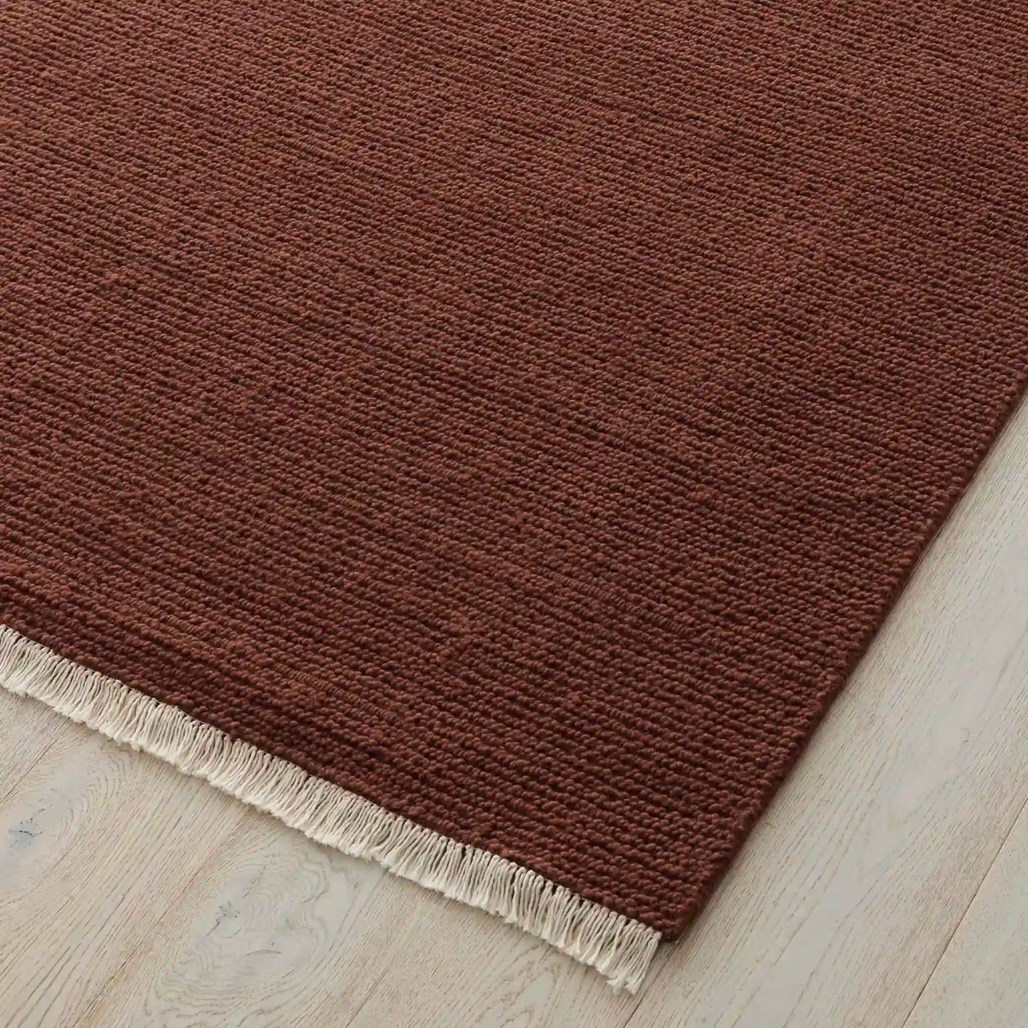 Brown rug with a white fringe on a wooden floor