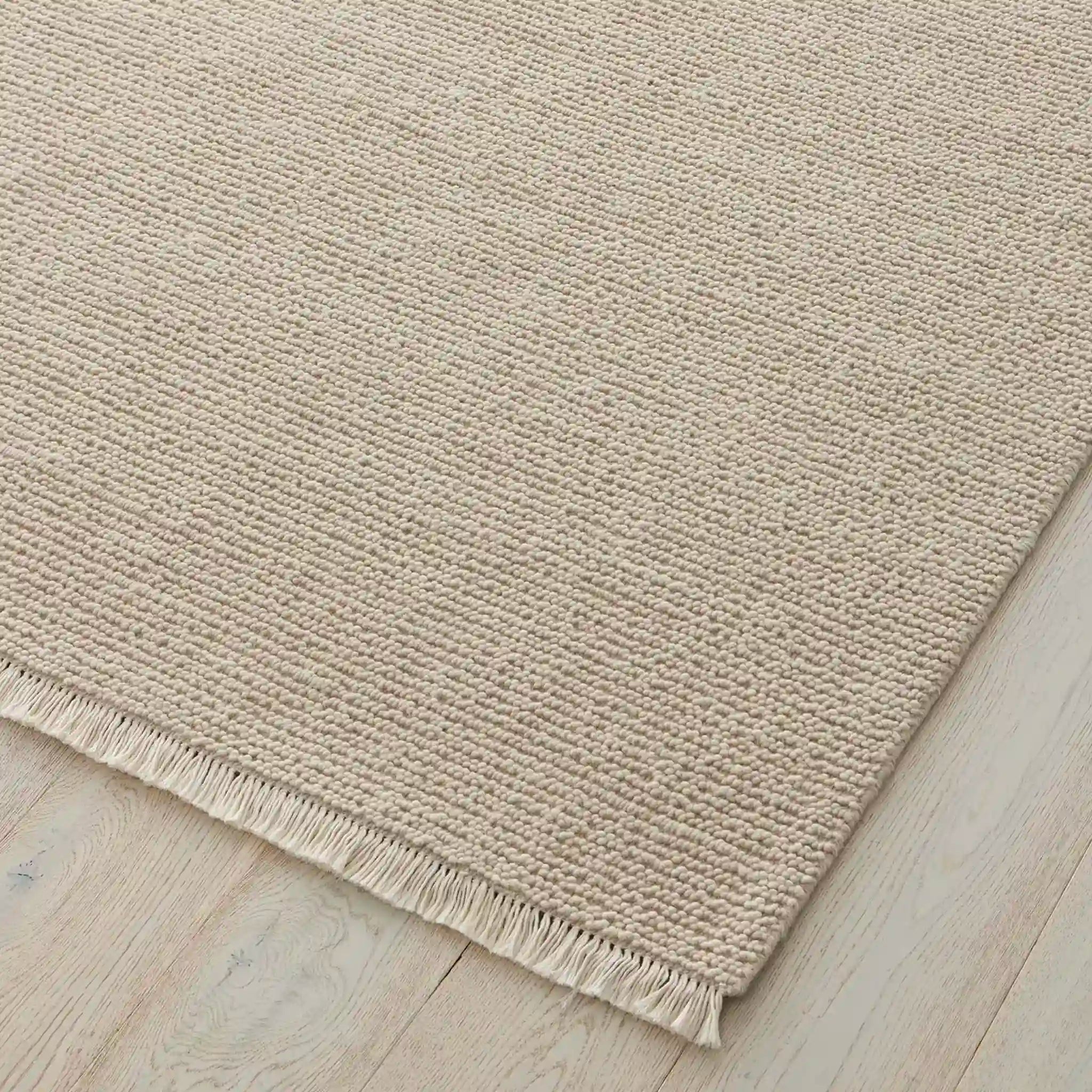 Beige rug with fringes on a wooden floor