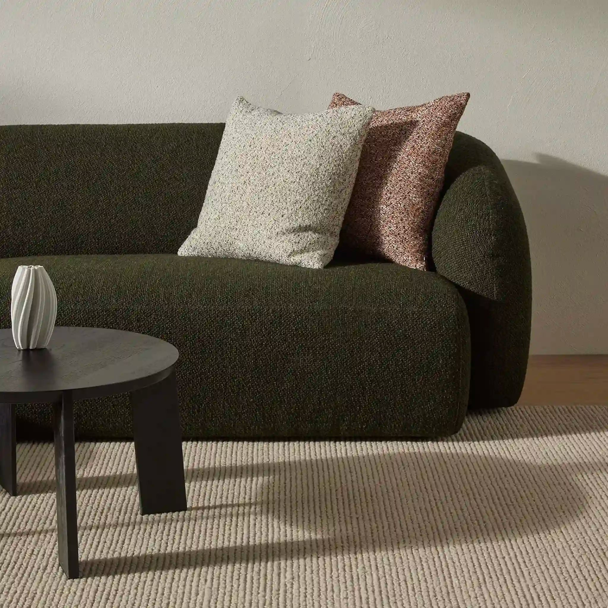 Dark green sofa with patterned cushions in a room with a neutral color scheme.