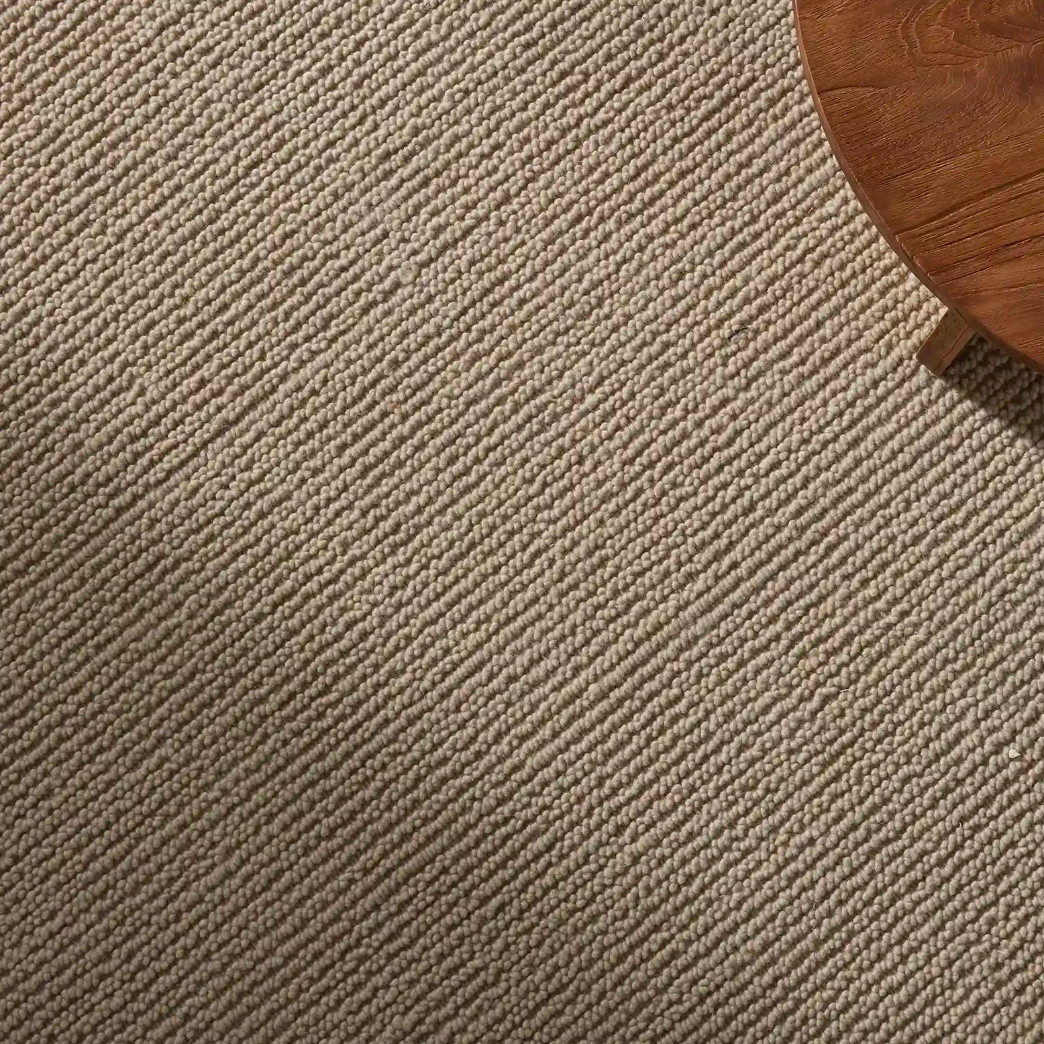 Close-up of a textured beige carpet with a wooden table corner.