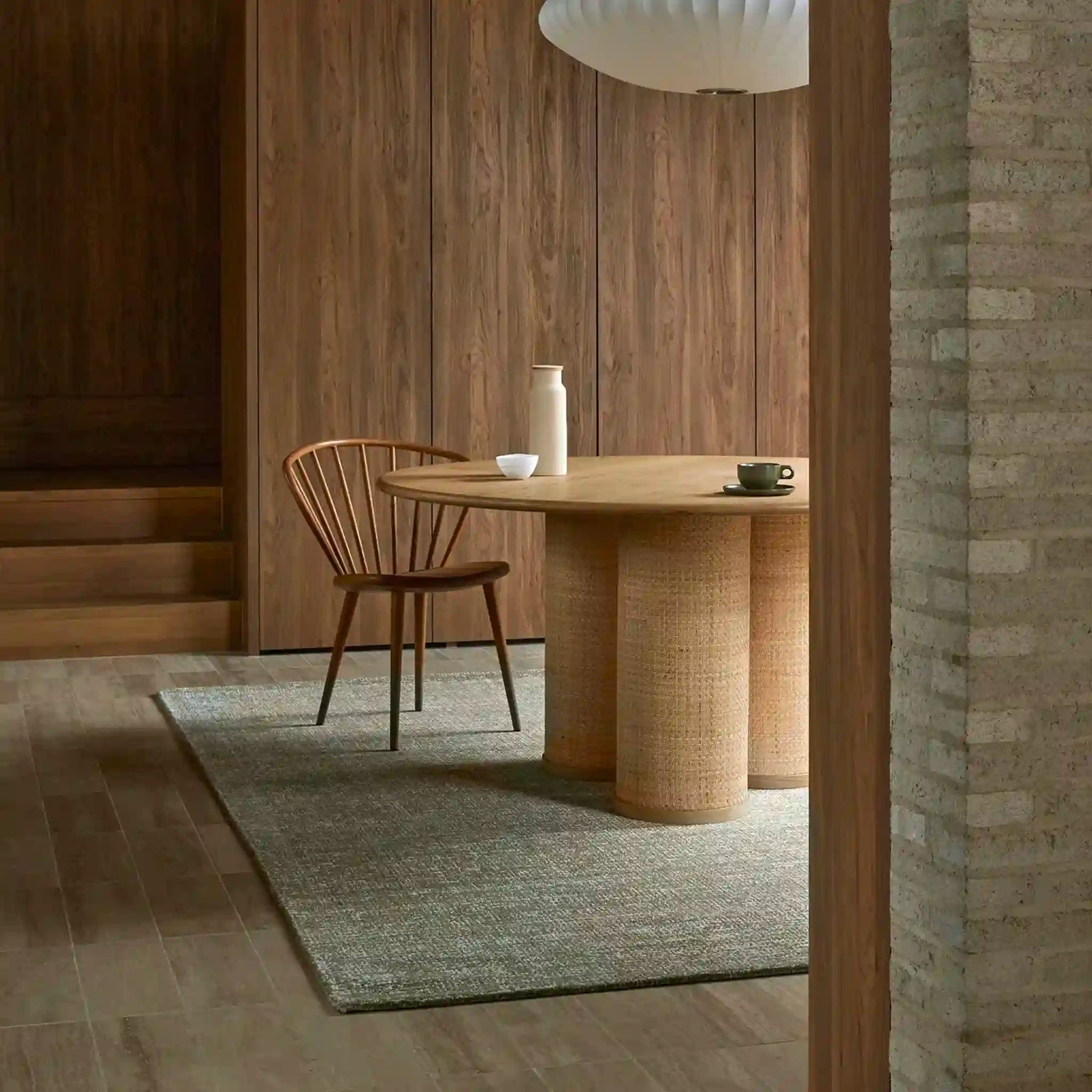 Dining area with a wooden table and chair in a room with wooden walls and a brick wall.