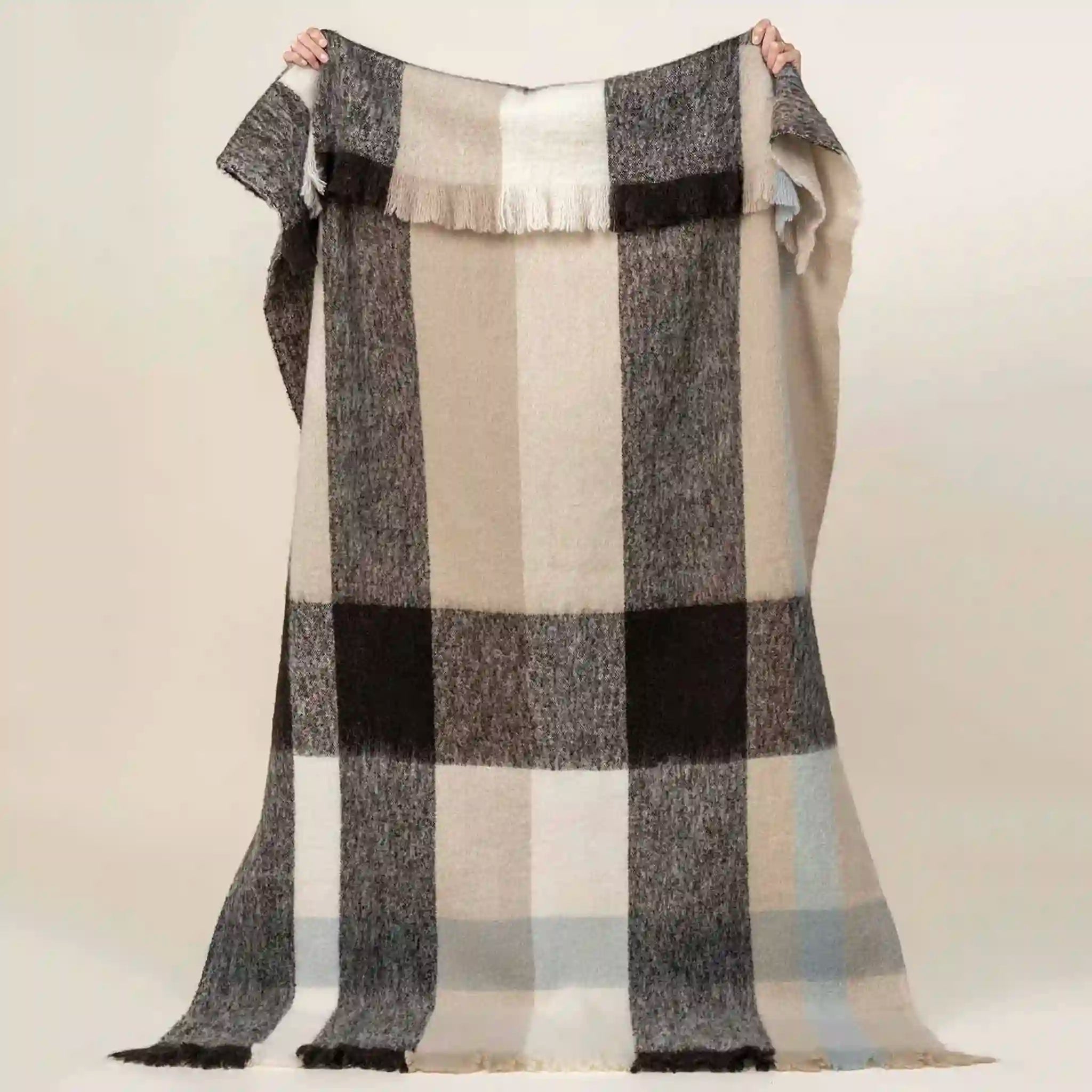 Plaid blanket with black, gray, and beige colors on a plain background