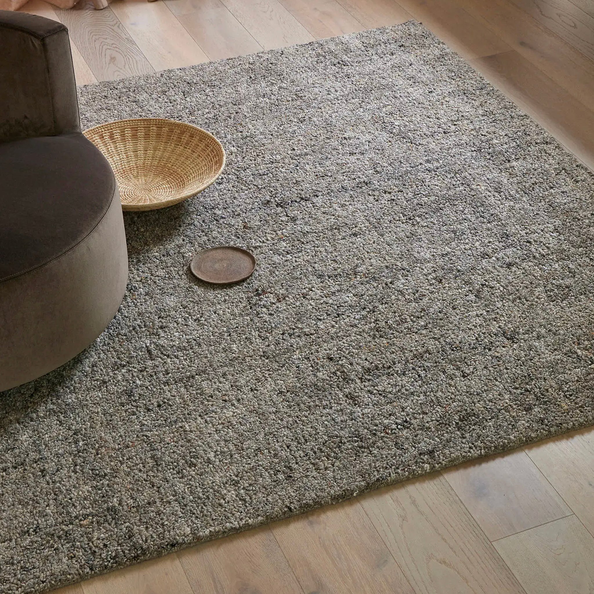 Gray textured rug on a wooden floor with a woven basket and brown ottoman.