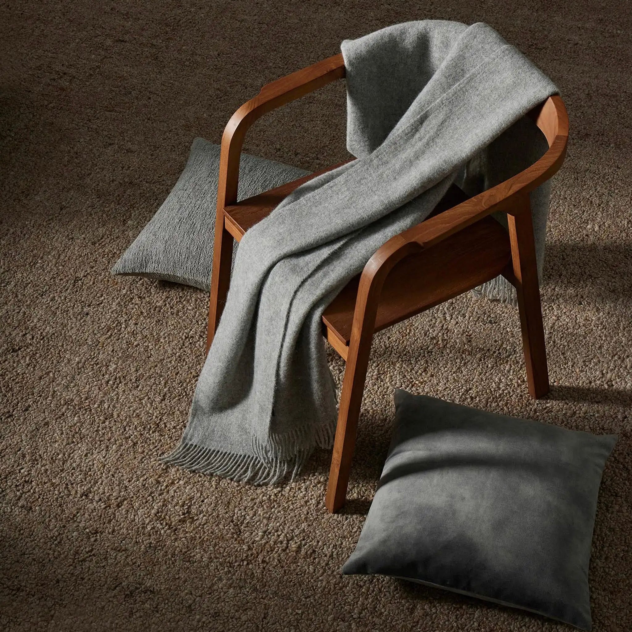 Gray blanket draped over a wooden chair with matching cushions on a brown carpet.