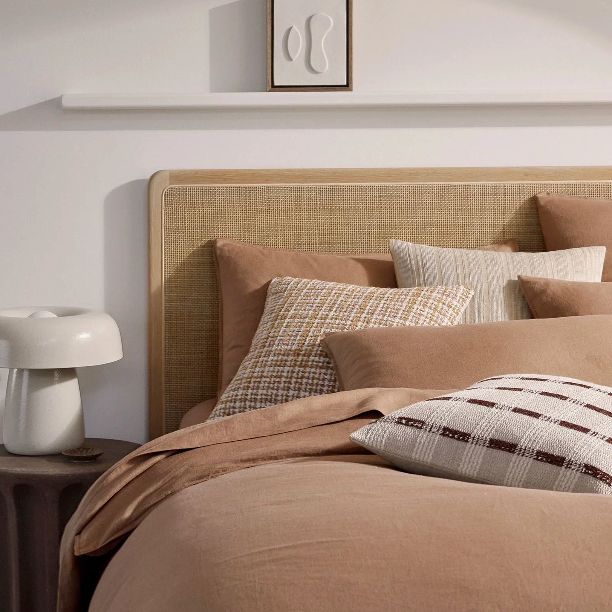 Bedroom with a bed featuring brown bedding and pillows, next to a nightstand with a lamp.