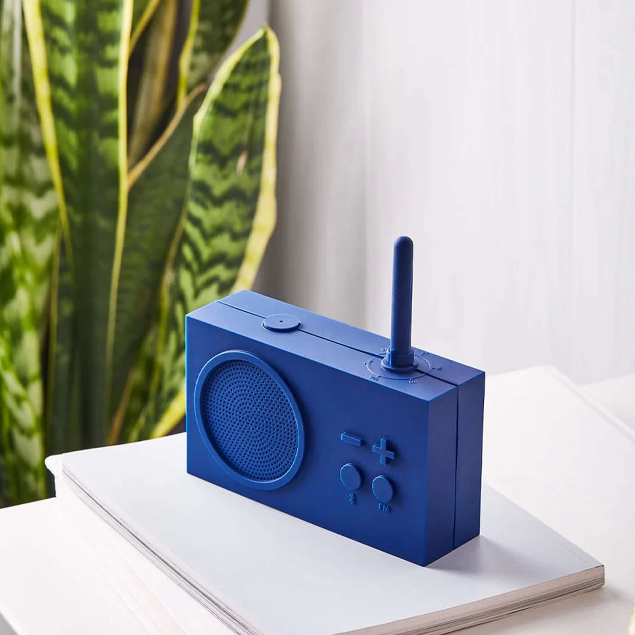 Lexon TYKHO 3 FM Radio & Bluetooth Speaker - Dark Blue on a table with greenery in the background.