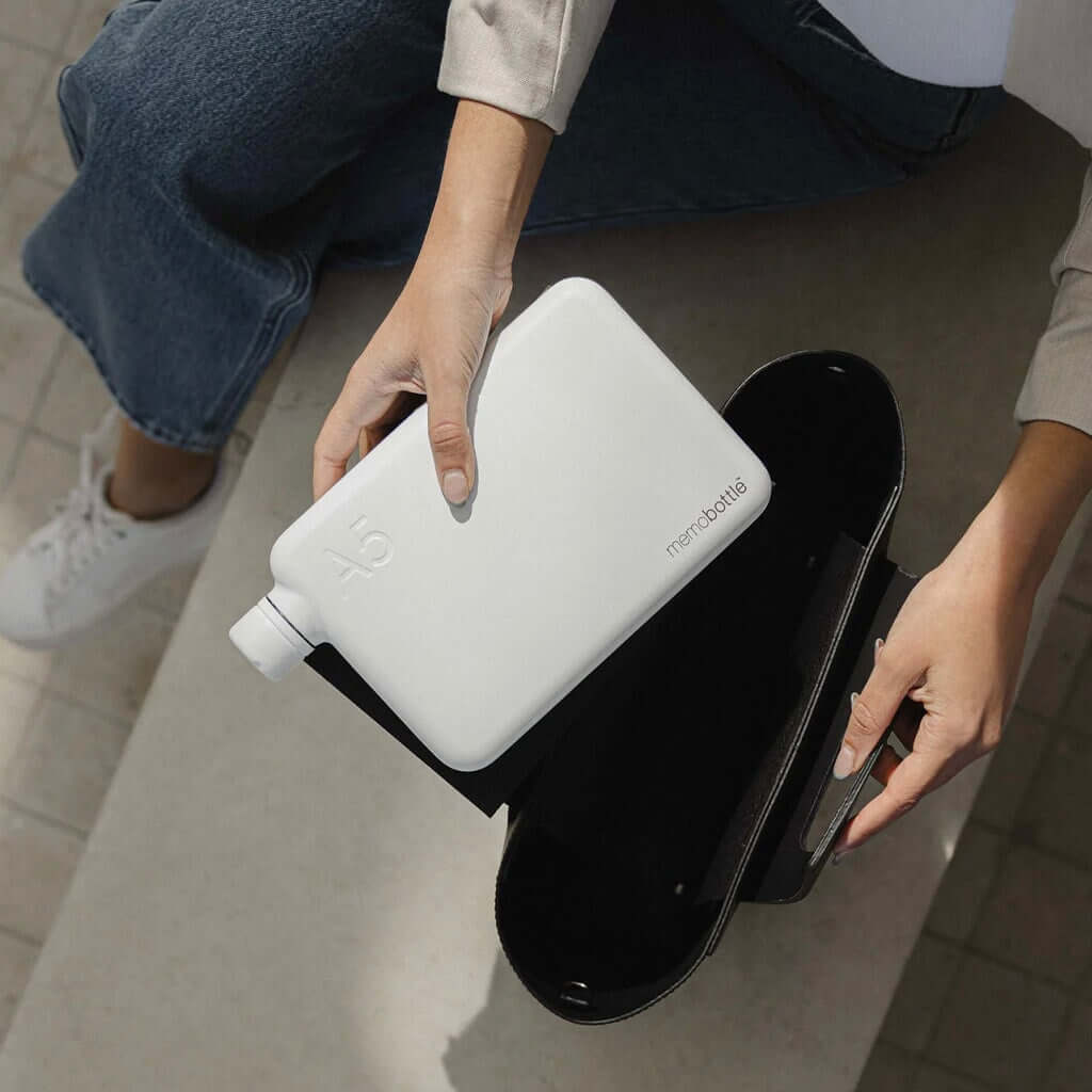 Alt Tag: Memobottle A5 Stainless Steel - White flat water bottle held above open bag, space-saving paper-inspired design